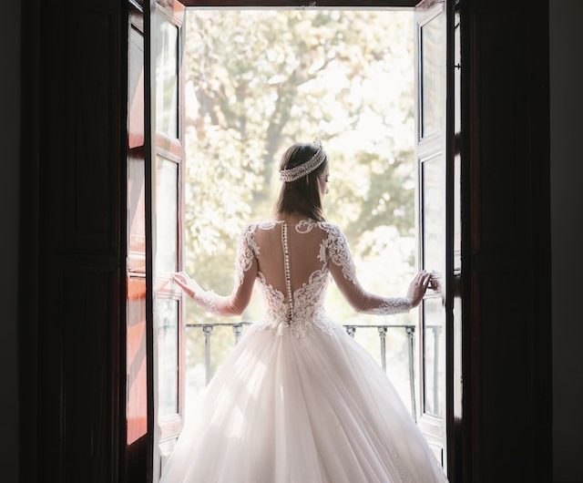 bride in wedding dress standing by window